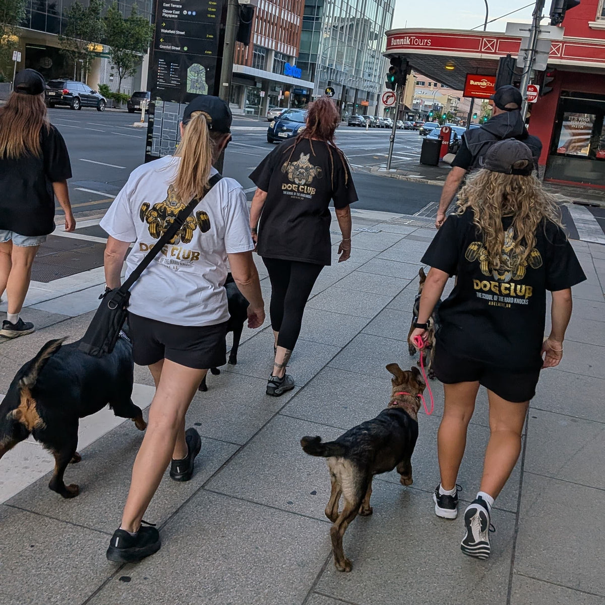 People walking dogs on a city street with modern buildings in the background