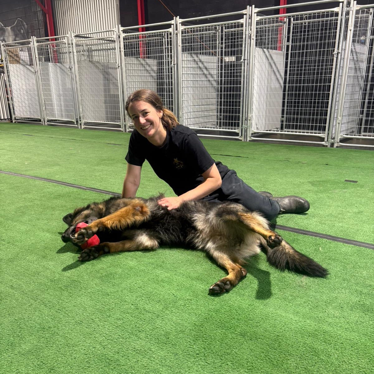 Person lying on the ground with a dog playing with a red toy in an indoor facility