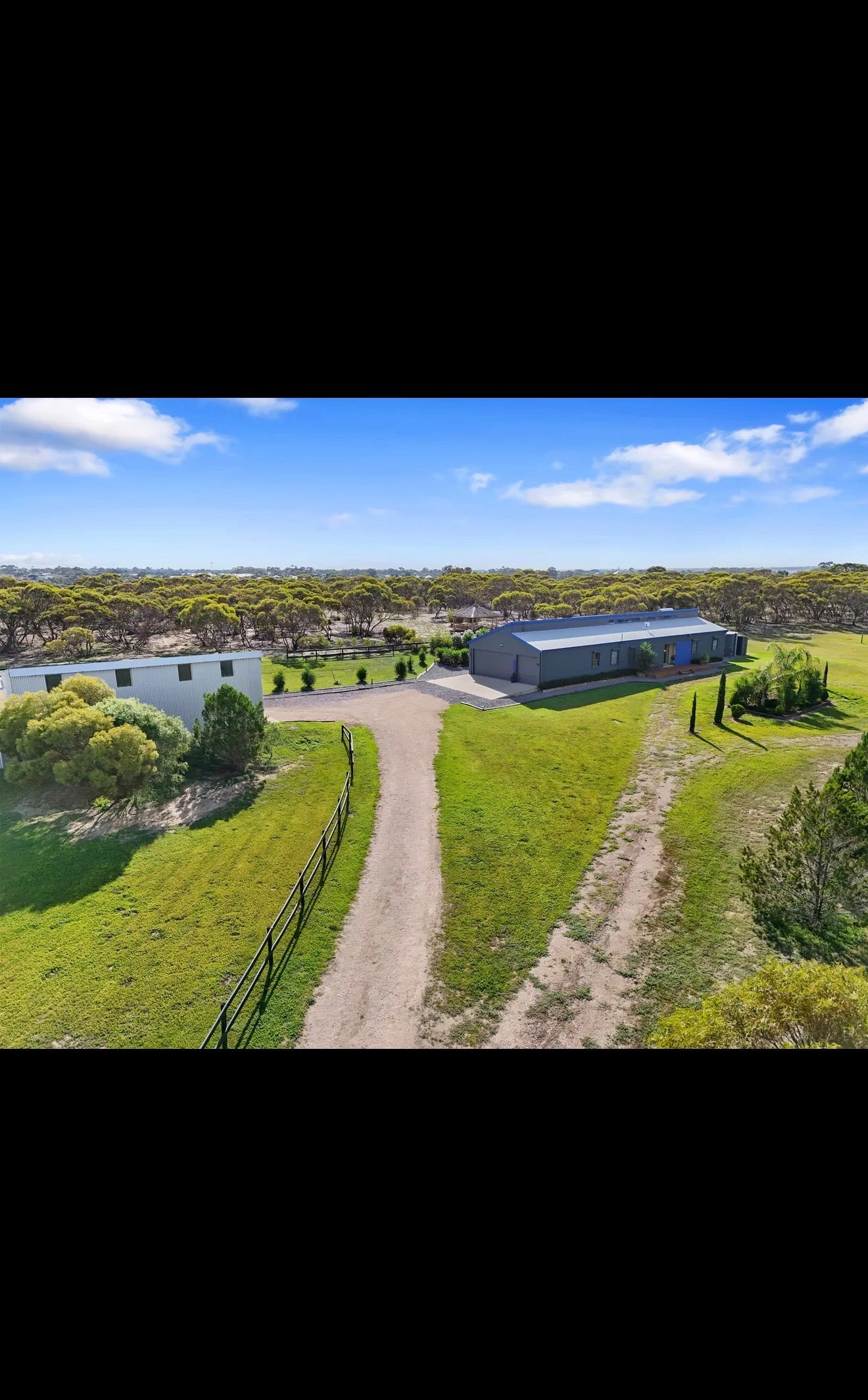 Aerial view of a large industrial building with surrounding greenery and clear sky.