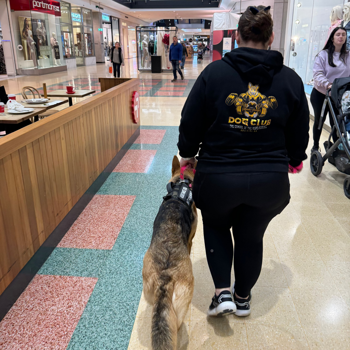 A dog and trainer walking through a shopping mall.